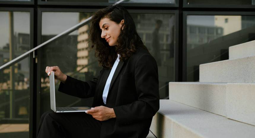A woman with a laptop on the steps of a glass building