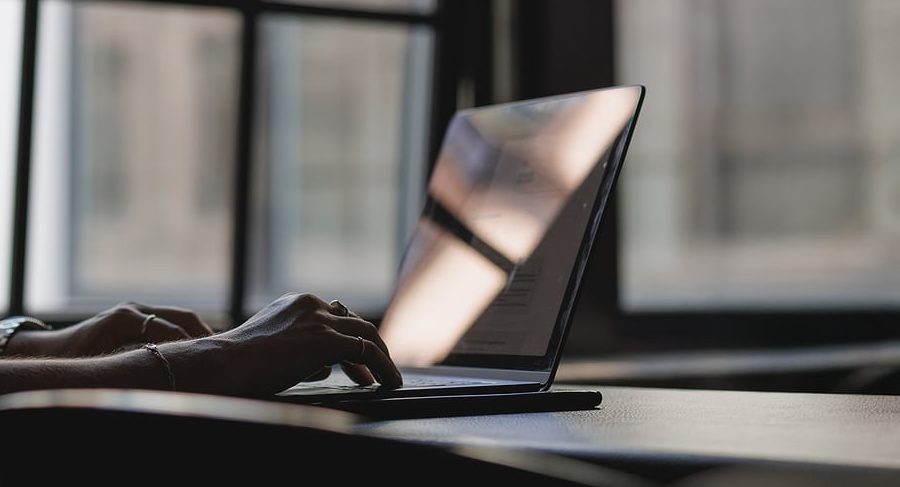 Hands typing on a laptop at a desk by a bright office window